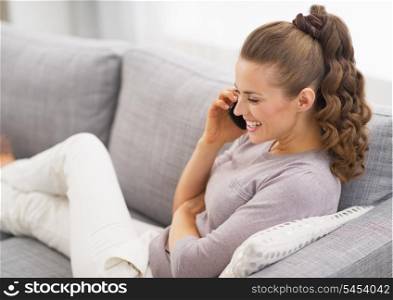 Smiling young woman laying on sofa and talking mobile phone