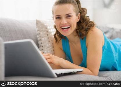 Smiling young woman laying on sofa with laptop