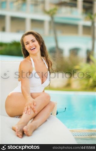 Smiling young woman laying on sunbed at poolside