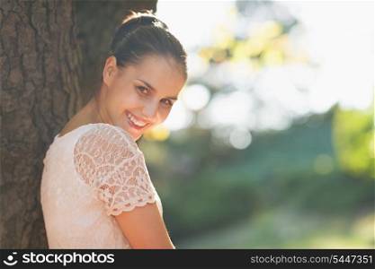 Smiling young woman lean against tree