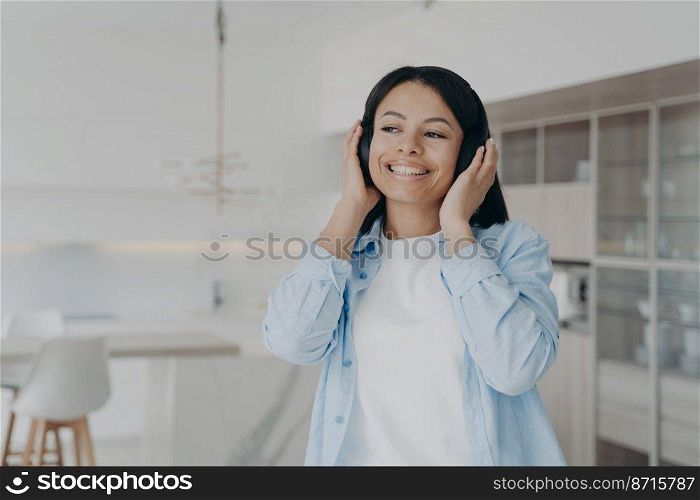 Smiling young woman listening to musical playlist in wireless headphones, enjoying music sound. Happy female listens to podcast, audio book or positive audio affirmations, resting at home. . Smiling woman listening to music in wireless headphones, enjoying musical sound resting at home