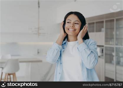 Smiling young woman listening to musical playlist in wireless headphones, enjoying music sound. Happy female listens to podcast, audio book or positive audio affirmations, resting at home. . Smiling woman listening to music in wireless headphones, enjoying musical sound resting at home