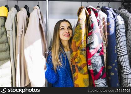 smiling young woman looking coats hanging rack