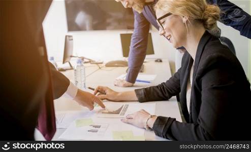 smiling young woman looking graph pointed by her colleague table