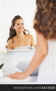 Smiling young woman looking in mirror in bathroom