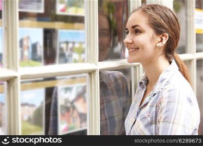 Smiling Young Woman Looking In Window Of Estate Agents