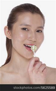 Smiling young woman looking into camera and licking a lollipop, studio shot