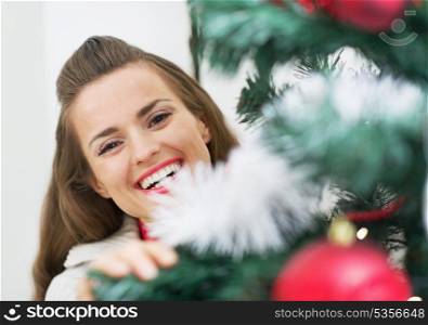 Smiling young woman looking out from christmas tree