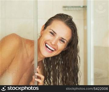 Smiling young woman looking out from shower cabin