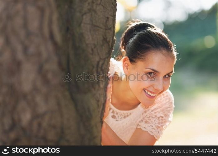 Smiling young woman looking out from tree