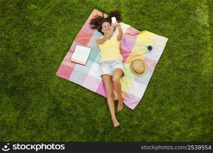 Smiling young woman lying on a blanket and making a selfie