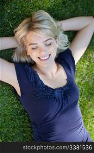 Smiling young woman lying on grass with eyes closed
