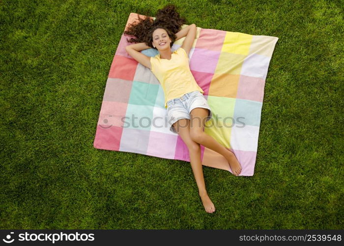 Smiling young woman lying on her back on a blanket and relaxing