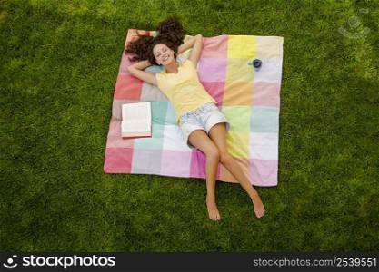 Smiling young woman lying on her back on a blanket and relaxing