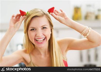 Smiling young woman making horns with strawberries