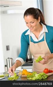 Smiling young woman making salad vegetables preparing meal kitchen