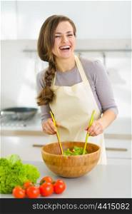 Smiling young woman mixing fresh salad