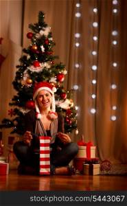 Smiling young woman near Christmas tree opening Christmas present&#xA;