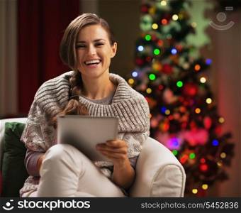 Smiling young woman near christmas tree using tablet pc