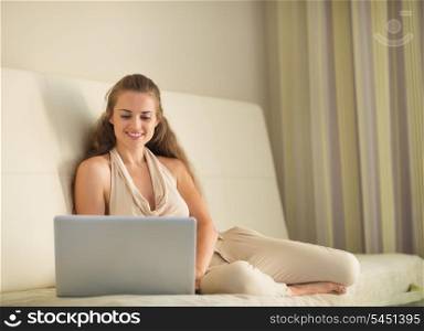 Smiling young woman on sofa with on laptop