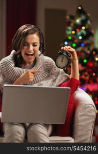 Smiling young woman pointing on clock while having video chat in front of christmas tree