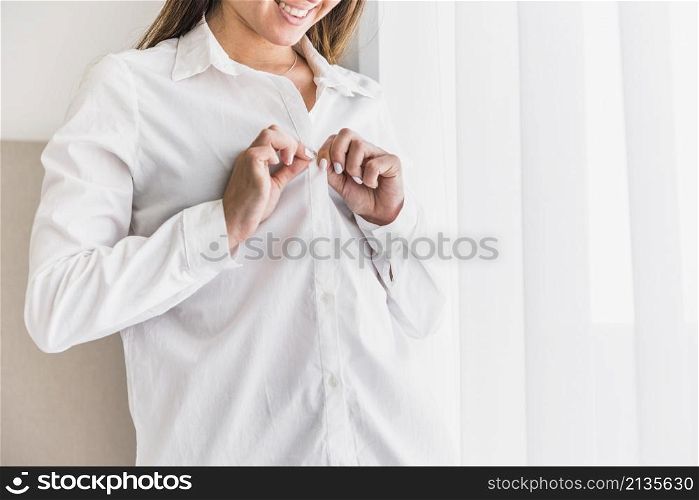 smiling young woman putting button her white shirt