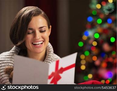 Smiling young woman reading christmas postcard in front of christmas lights