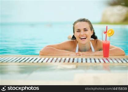Smiling young woman relaxing in pool with cocktail