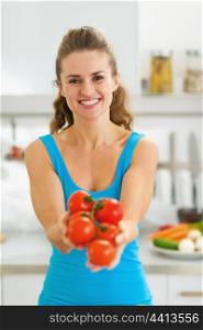 Smiling young woman showing bunch of tomato in modern kitchen