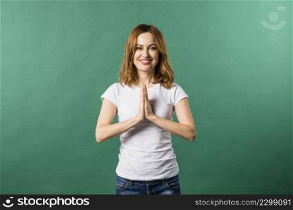 smiling young woman showing namaste gesture against green backdrop