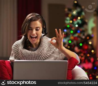 Smiling young woman showing ok gesture while having video chat in front of christmas tree