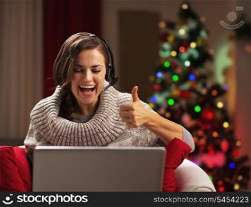 Smiling young woman showing thumbs up while having video chat in front of christmas tree