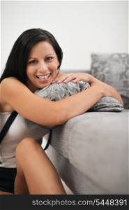 Smiling young woman sitting near sofa and embracing pillow