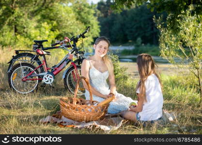 Smiling young woman sitting on blanket under big tree with her daughter