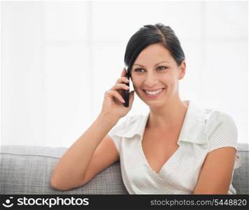 Smiling young woman sitting on couch and talking cell phone