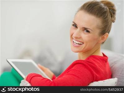 Smiling young woman sitting on couch and using tablet pc