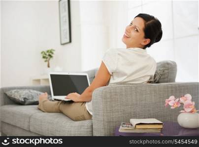 Smiling young woman sitting on couch and working on laptop