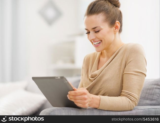 Smiling young woman sitting on couch and working on tablet pc