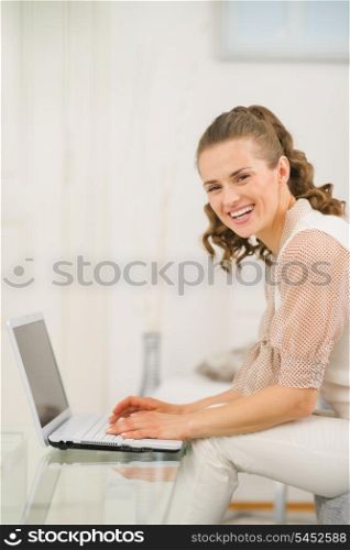 Smiling young woman sitting on couch in living room and using laptop