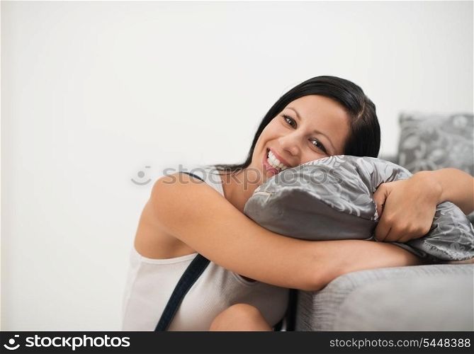 Smiling young woman sitting on floor and embracing pillow