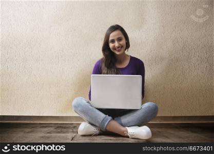 Smiling young woman sitting on floor using laptop