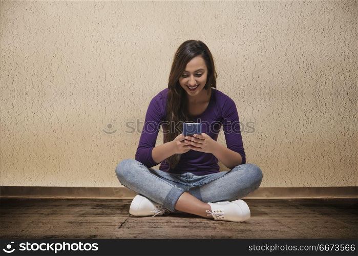 Smiling young woman sitting on floor using mobile phone