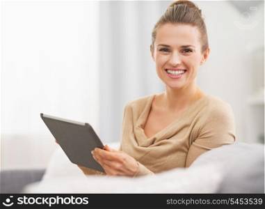 Smiling young woman sitting on sofa and using tablet pc