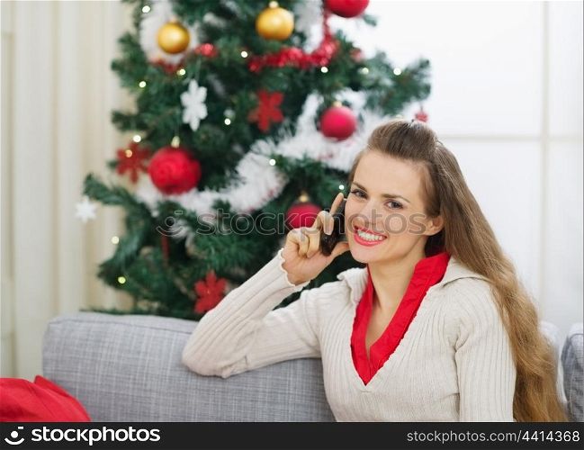 Smiling young woman speaking mobile phone near Christmas tree