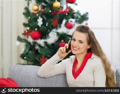 Smiling young woman speaking mobile phone near Christmas tree