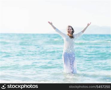 Smiling young woman standing in sea and sprinkling water