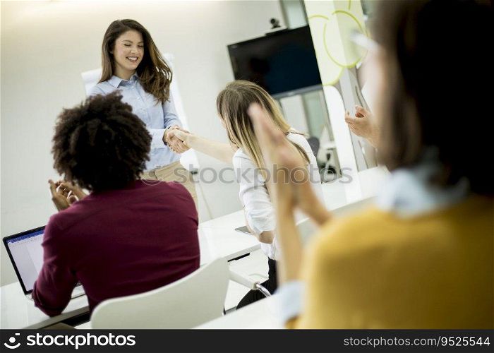 Smiling young woman standing near whiteboard and shaking hand to her female colleague in the small startup office