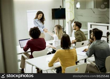 Smiling young woman standing near whiteboard and shaking hand to her female colleague in the small startup office