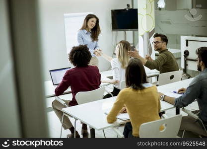 Smiling young woman standing near whiteboard and shaking hand to her female colleague in the small startup office