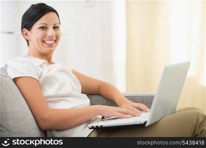 Smiling young woman surfing net on laptop in living room